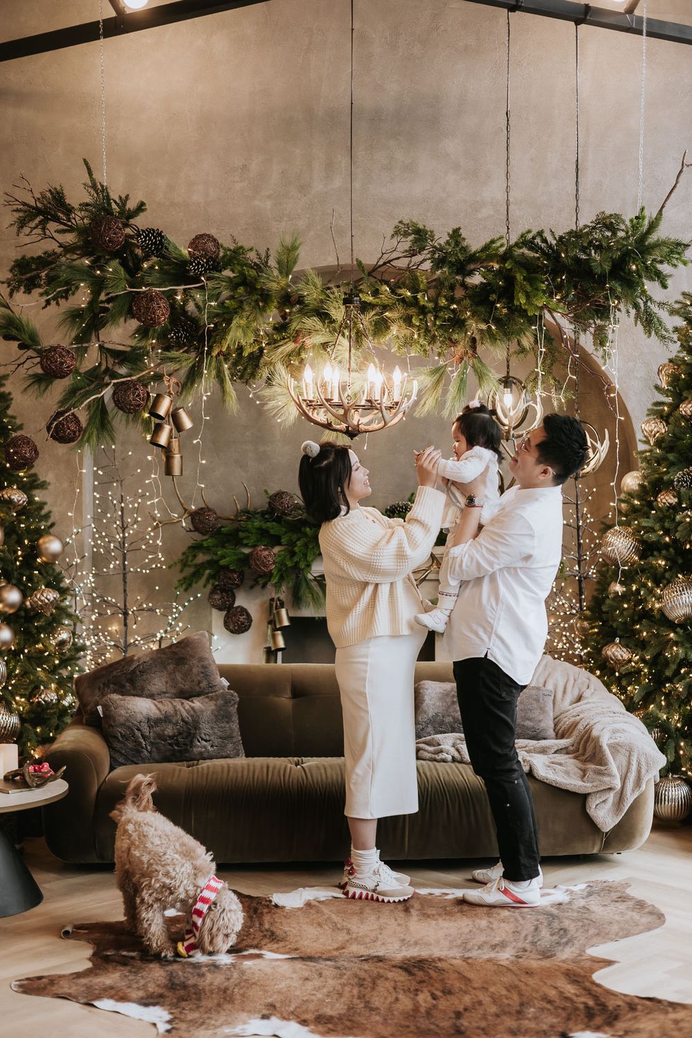 Family celebrates Christmas together in cozy living room with decorated evergreen garlands and glowing chandelier.