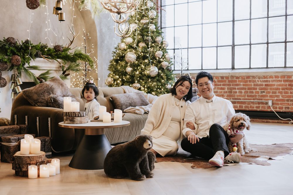 Cozy holiday scene with family and pets relaxing by decorated Christmas tree in modern loft space with exposed brick walls.
