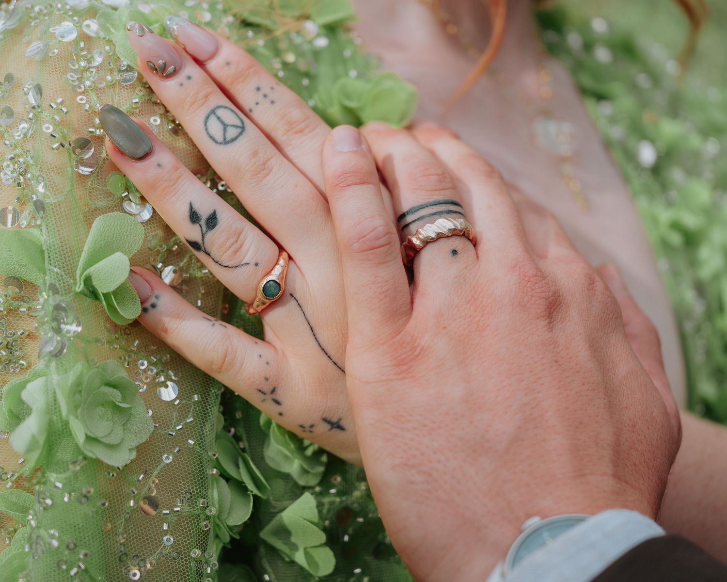 Close-up view of hands with rings resting on green foliage with small white flowers in the background.