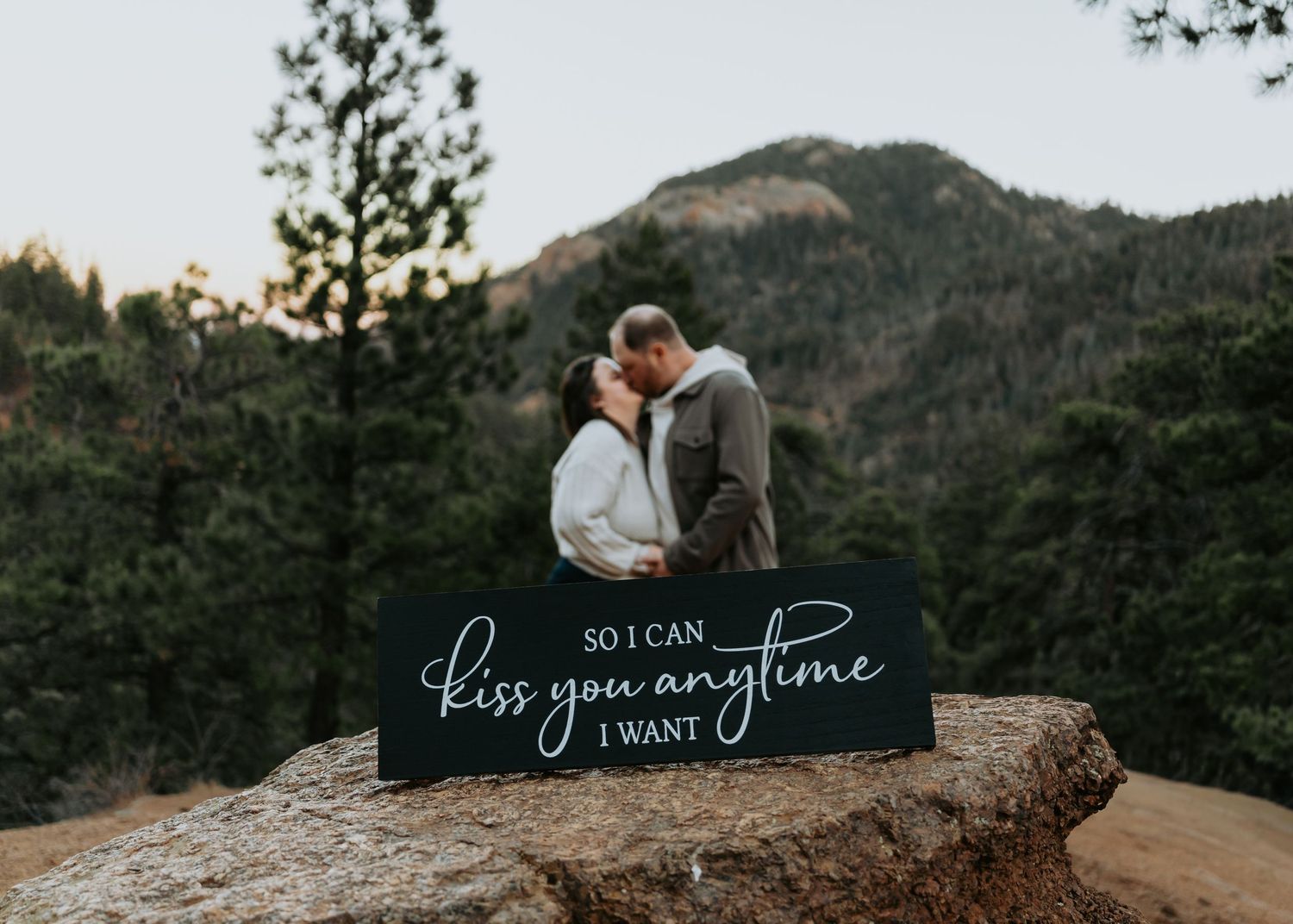 A couple shares a romantic embrace on a rocky mountain overlook during sunset.