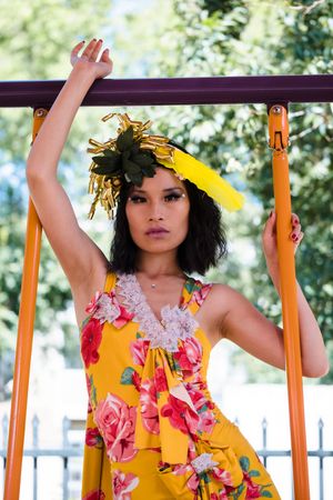 A person in a yellow floral dress and decorative headpiece poses on playground equipment outdoors. Vacaville fashion show.