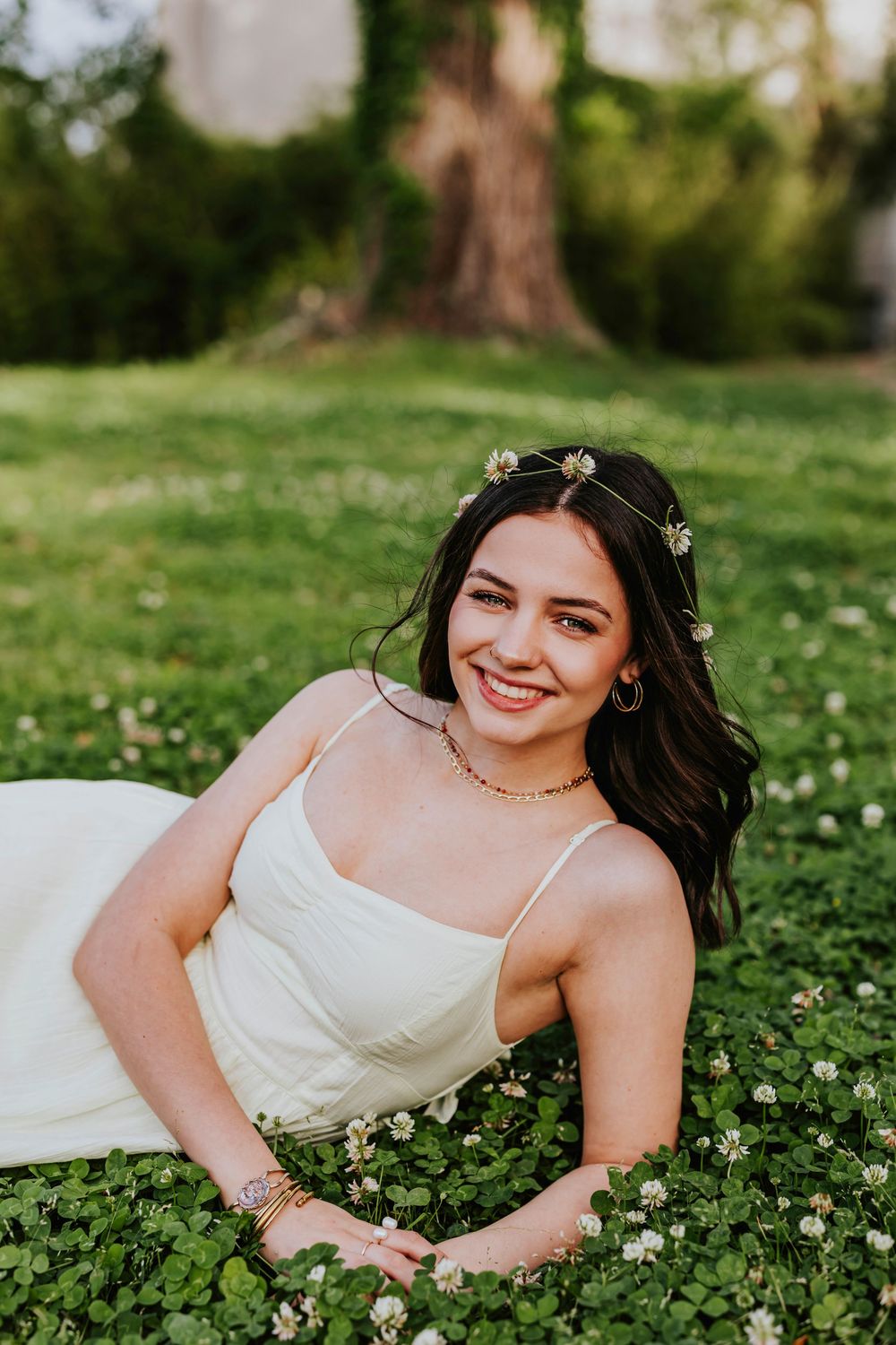 Ethereal spring portrait lying in clover-filled grass wearing a white dress and floral accessories.