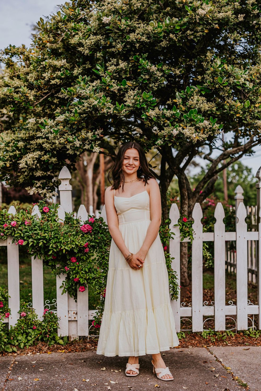 A cream-colored dress photographed against a white picket fence with blooming roses in the garden.
