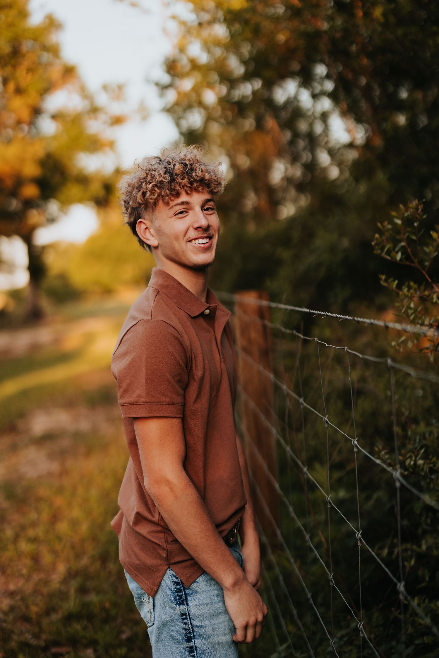 Autumn photoshoot in warm tones with rustic fence and fall foliage.