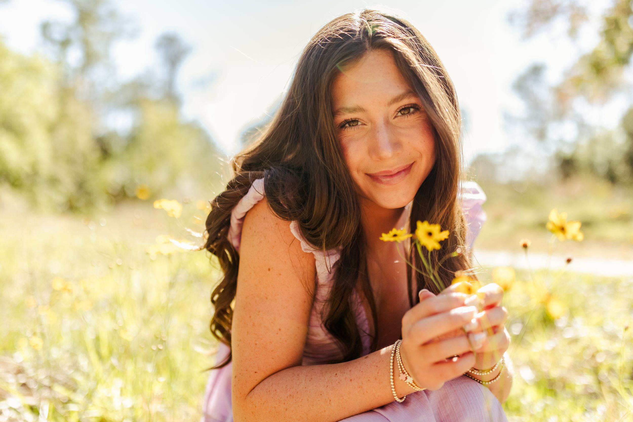 A person lying in a sunny wildflower meadow holds a yellow dandelion flower while relaxing in nature on a warm day.