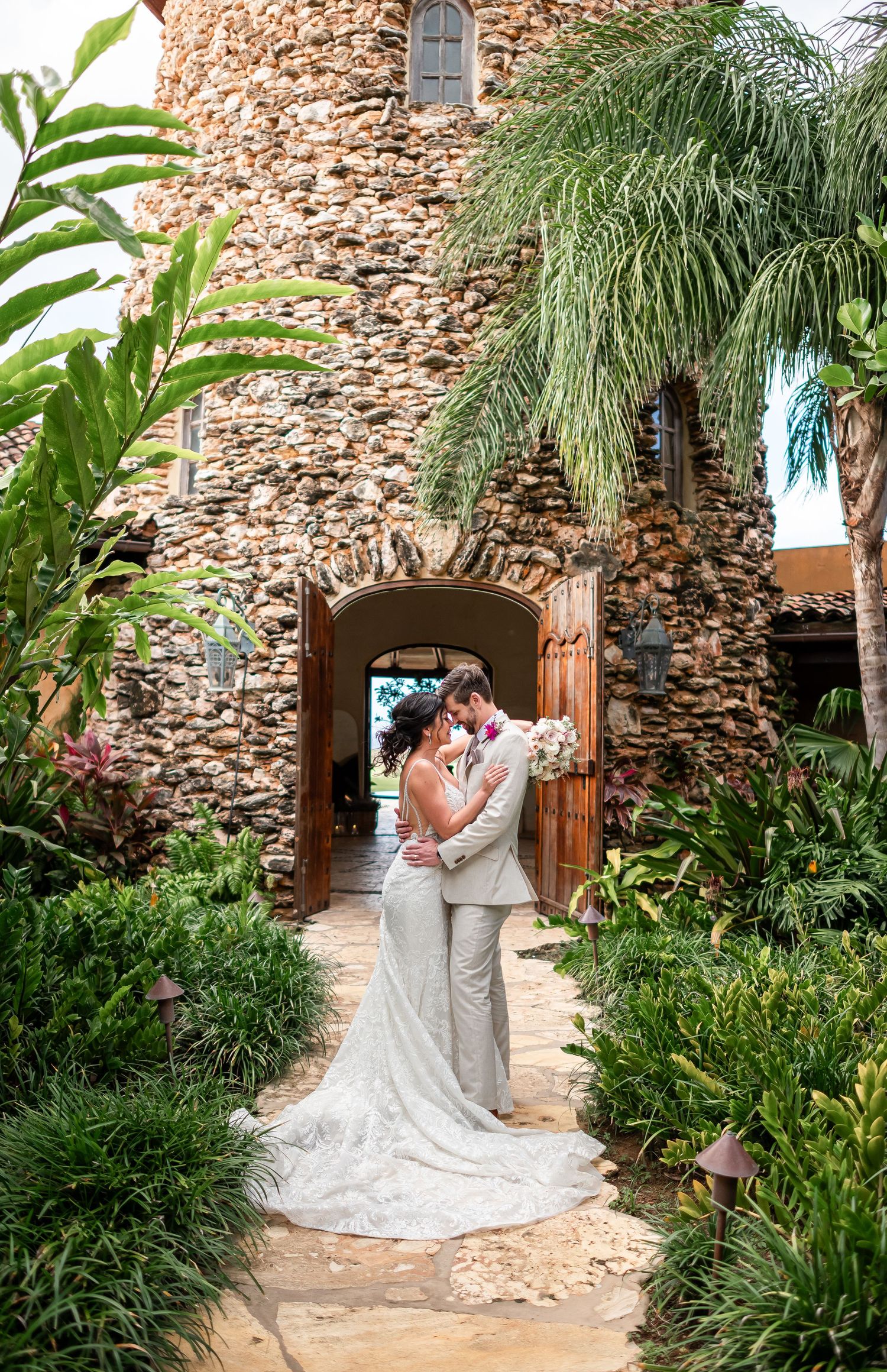 Elegant couple shares romantic moments in a rustic stone courtyard surrounded by lush tropical plants and palm trees in Royal Isabela Resort