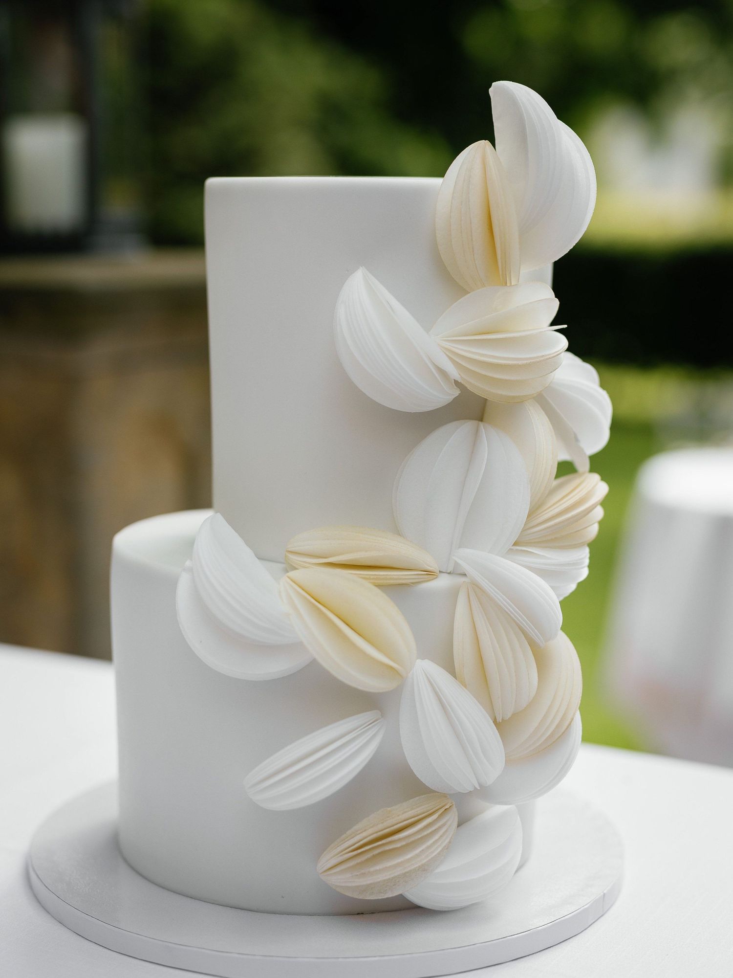 Close-up views of white wedding cake decorated with delicate sugar flower petals in cascading arrangement.