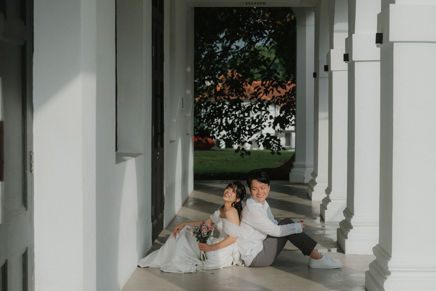 Elegant white columned walkway with couple in wedding attire posing against architectural backdrop.