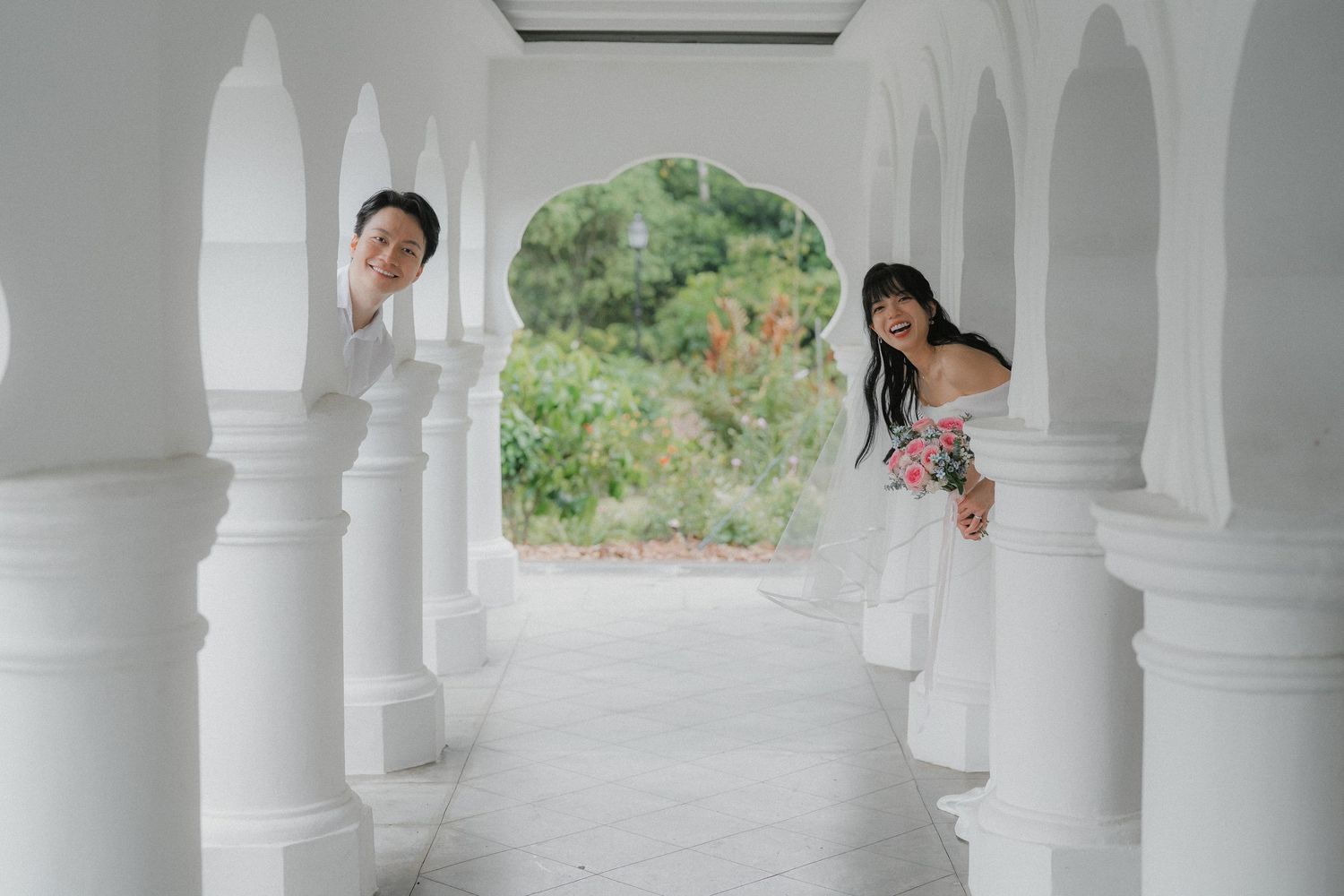 A playful couple poses between white pillars in an architectural setting.