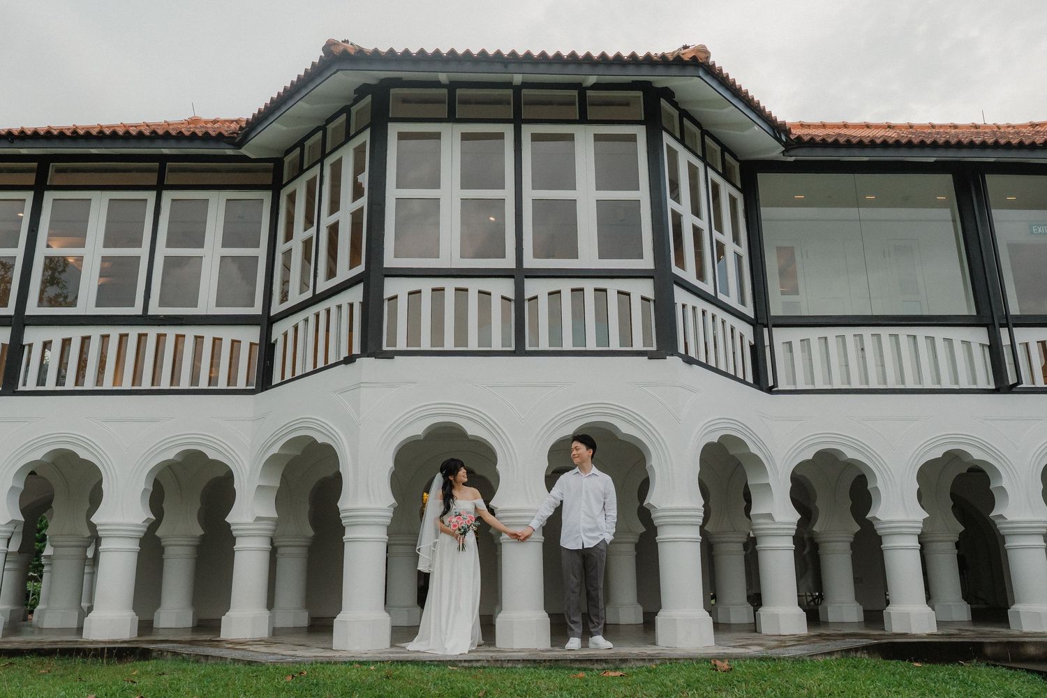 A couple stands under arched columns of a Spanish colonial style building.