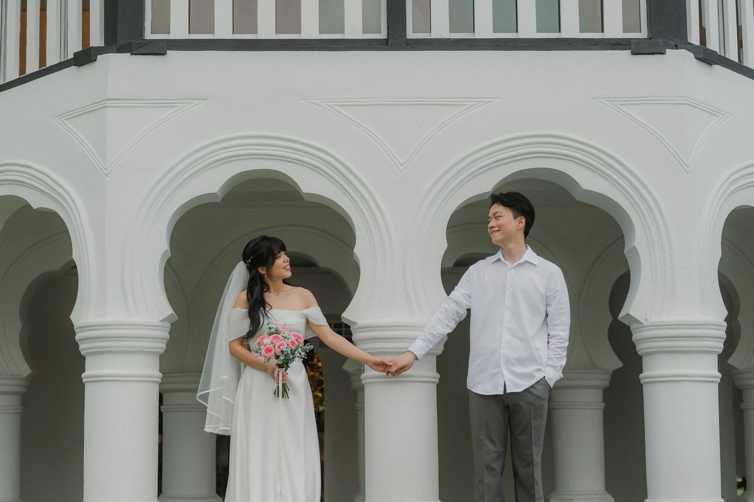 Elegant wedding portrait under white arched colonnade with couple holding hands.