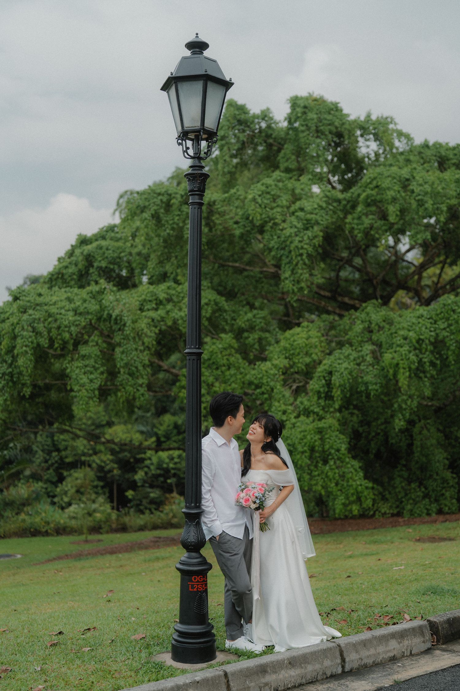 A couple poses beneath a vintage street lamp against lush greenery.