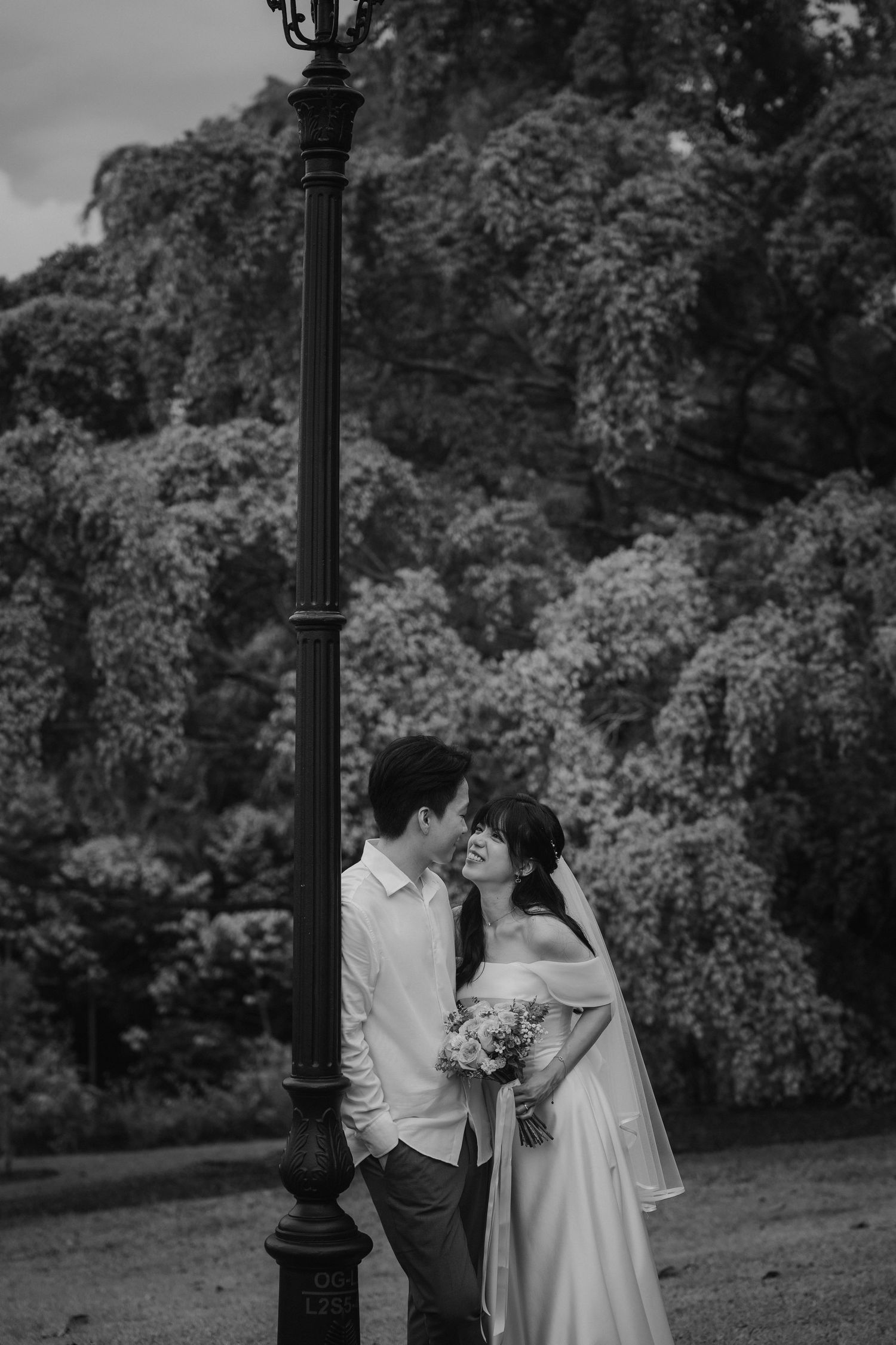 A romantic black and white wedding photo captured next to a vintage lamppost in a lush garden setting.
