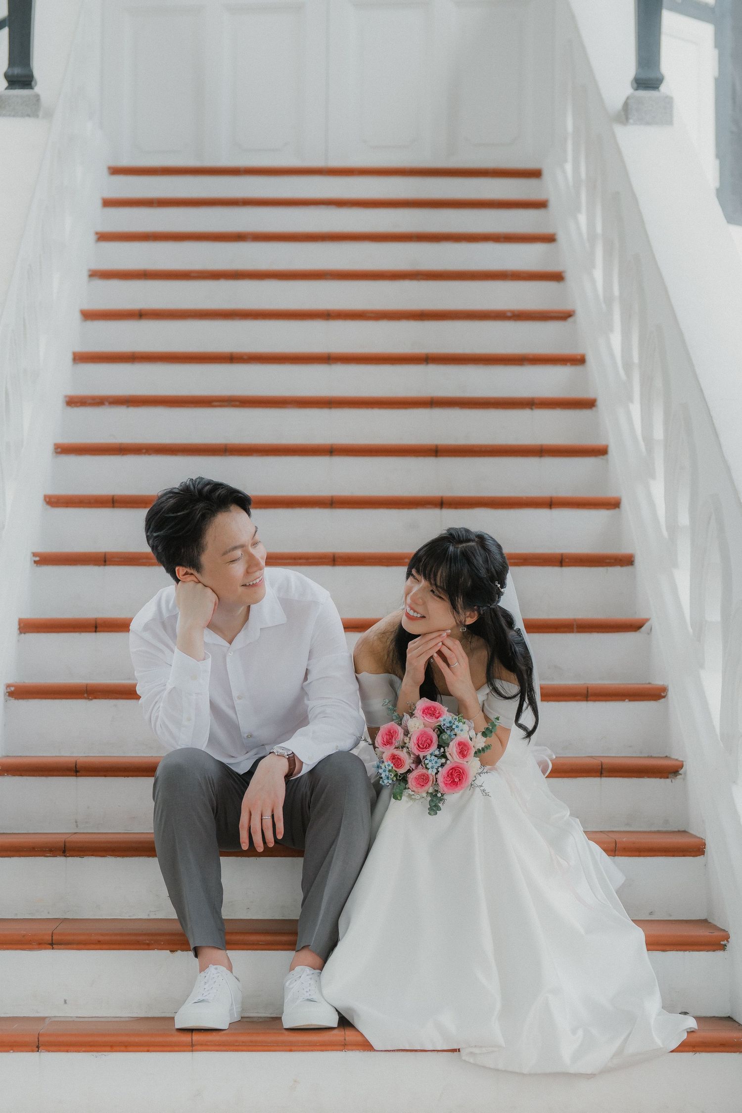 Wedding couple sitting on white staircase with orange steps sharing intimate moment.