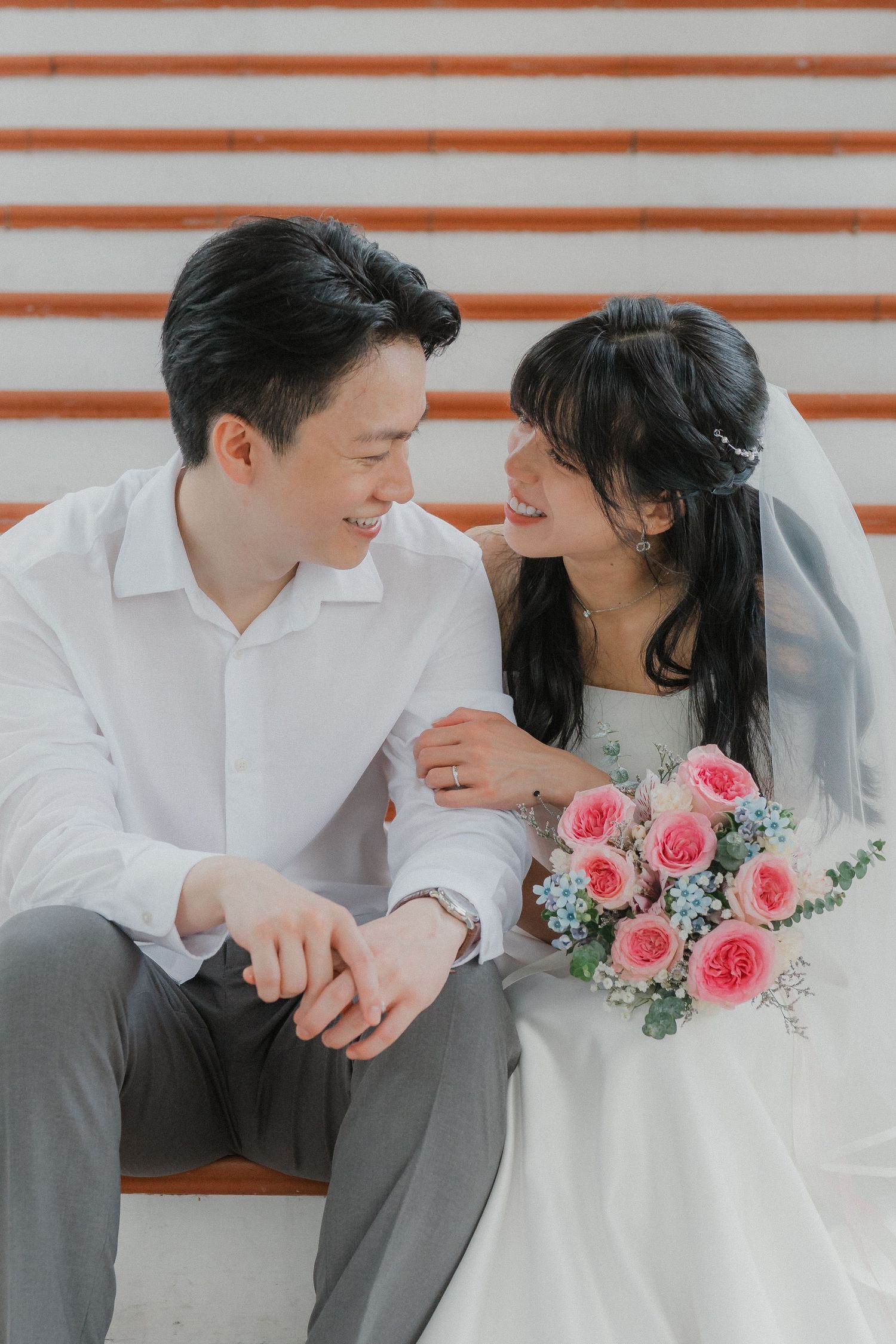 A sweet wedding moment captured on stairs with a pink rose bouquet and casual attire.