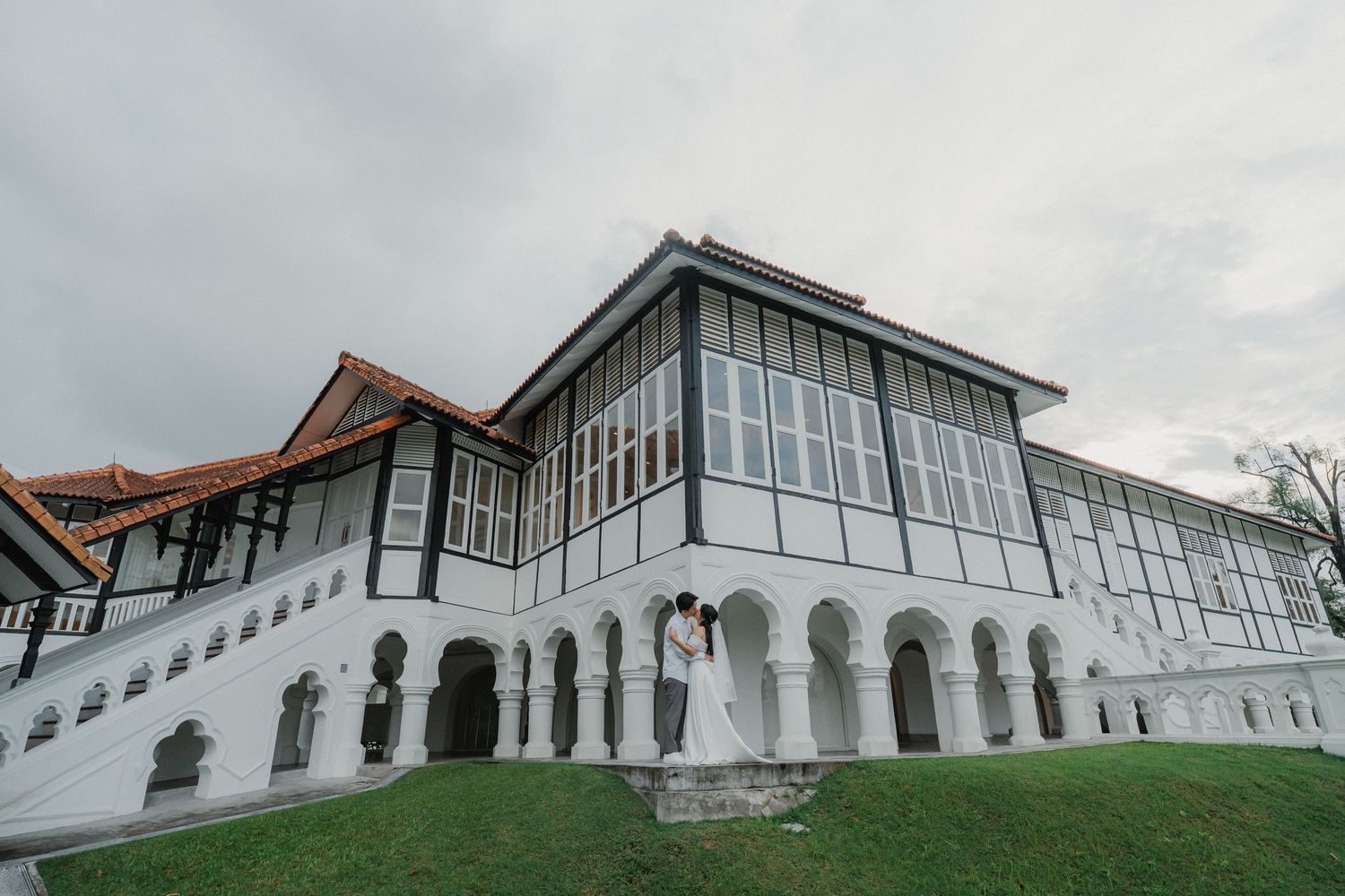 White colonial style building with arched columns and large glass windows against cloudy sky.