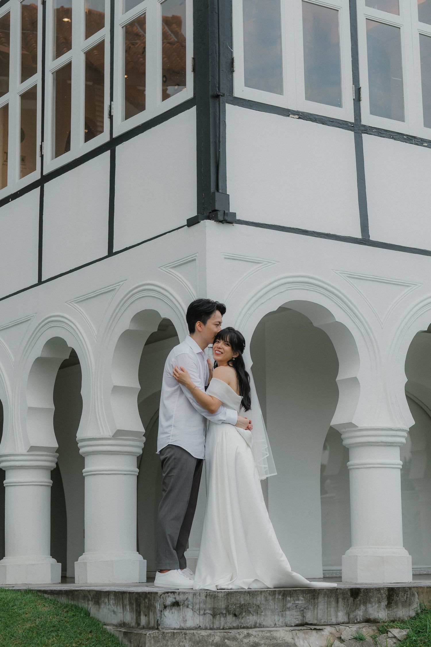 A romantic wedding portrait captured under white arched columns of a colonial building.