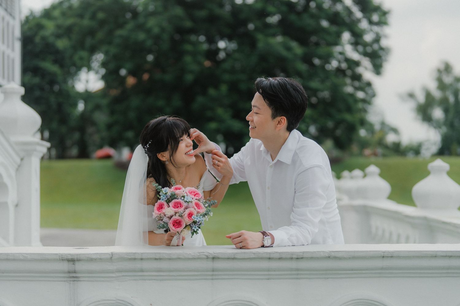 Romantic wedding portrait on white ornate balcony overlooking green gardens.