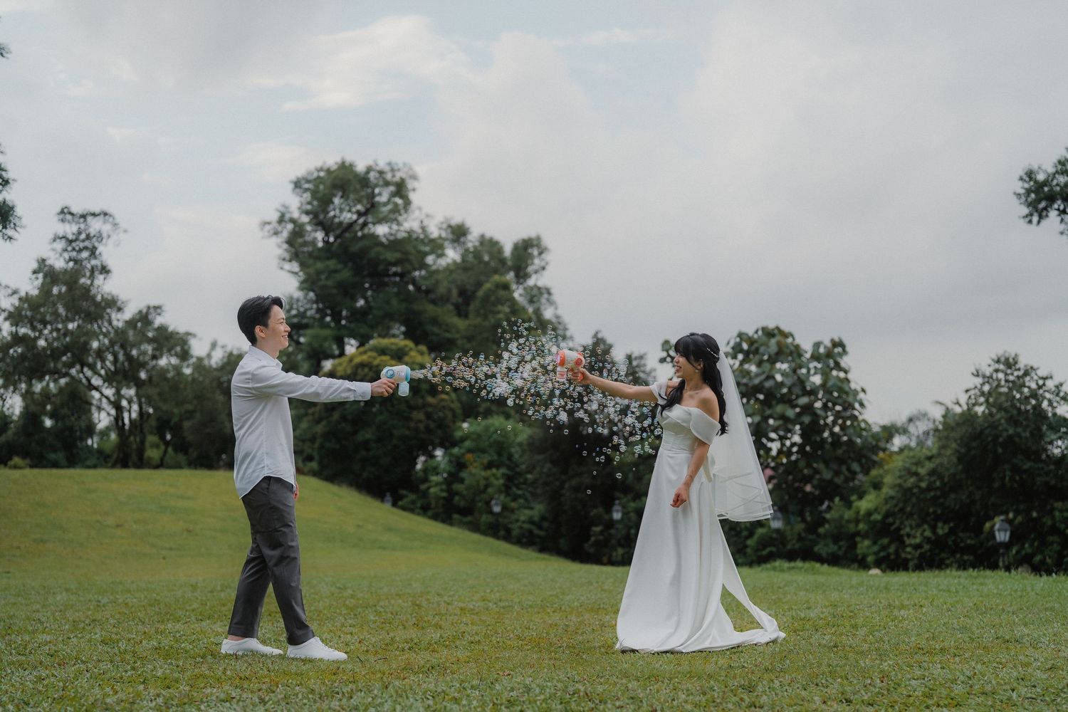 A couple in wedding attire playing together on a grassy hill.