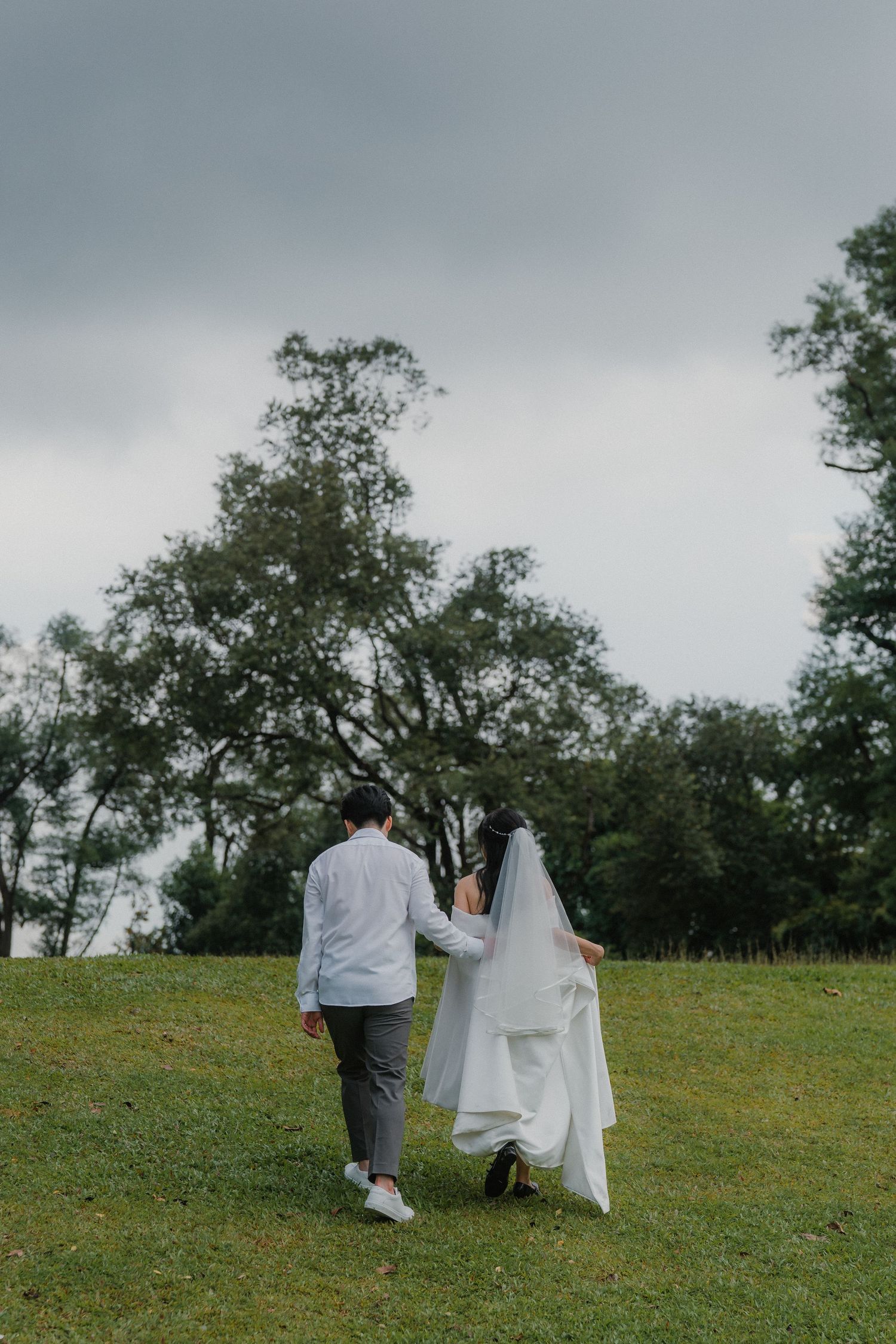 Two people walk together across a lush green hillside under cloudy skies.