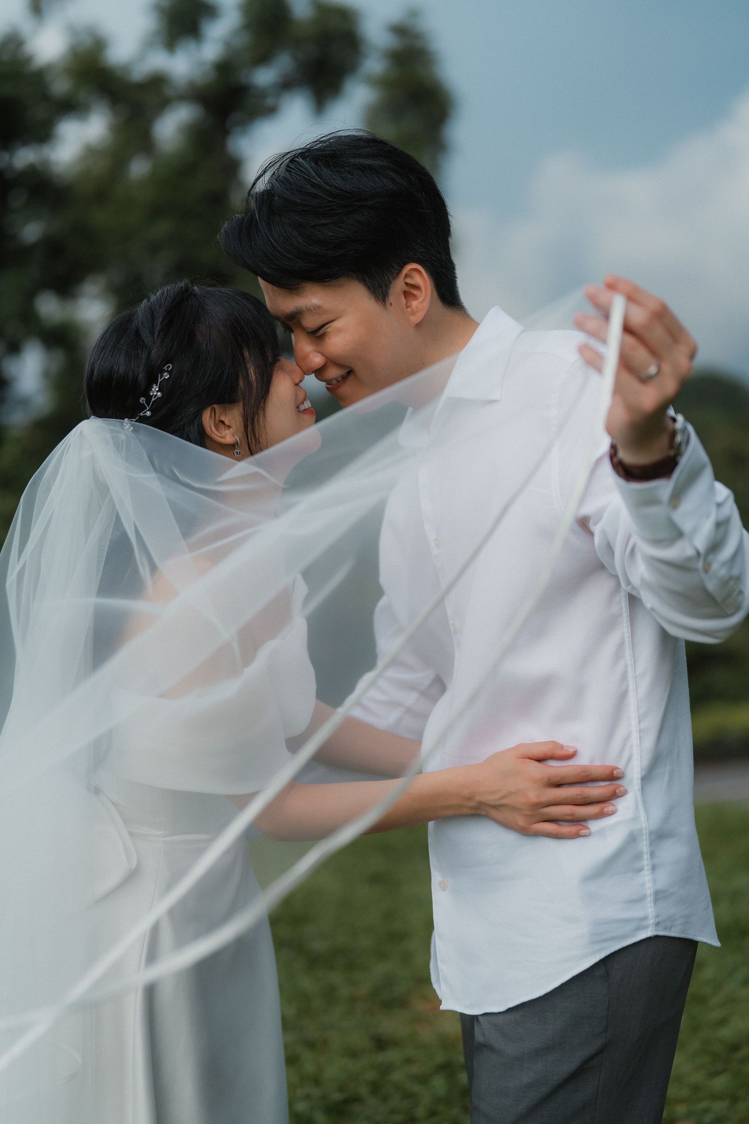 A tender moment captured as newlyweds share an intimate embrace with flowing white veil in natural setting.