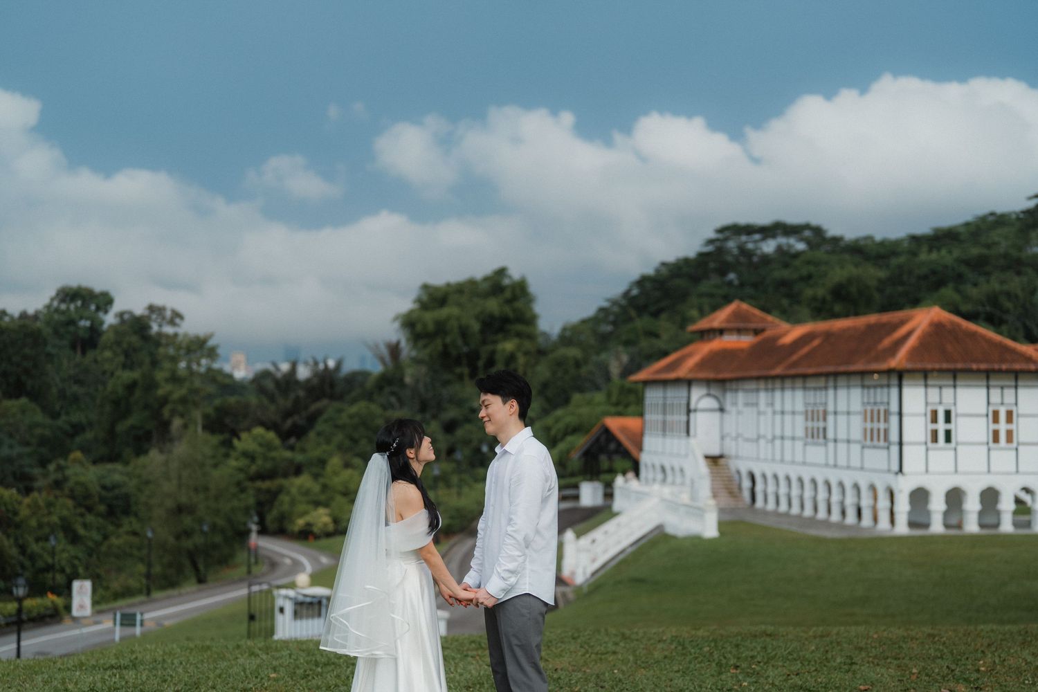 A wedding couple poses in front of a grand colonial building with orange roof tiles.