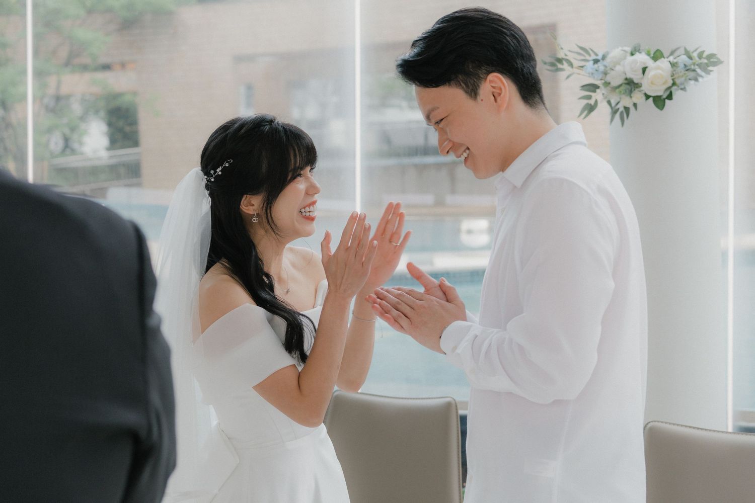Intimate indoor wedding ceremony with couple in white attire exchanging vows.