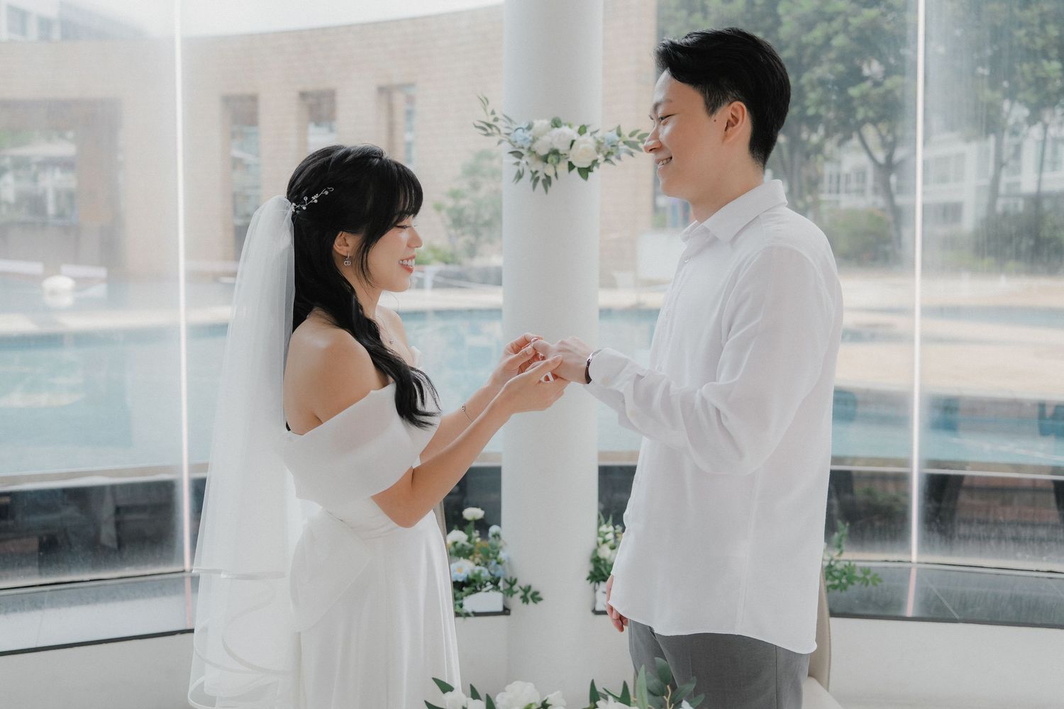A couple in white exchanging rings during their wedding ceremony.