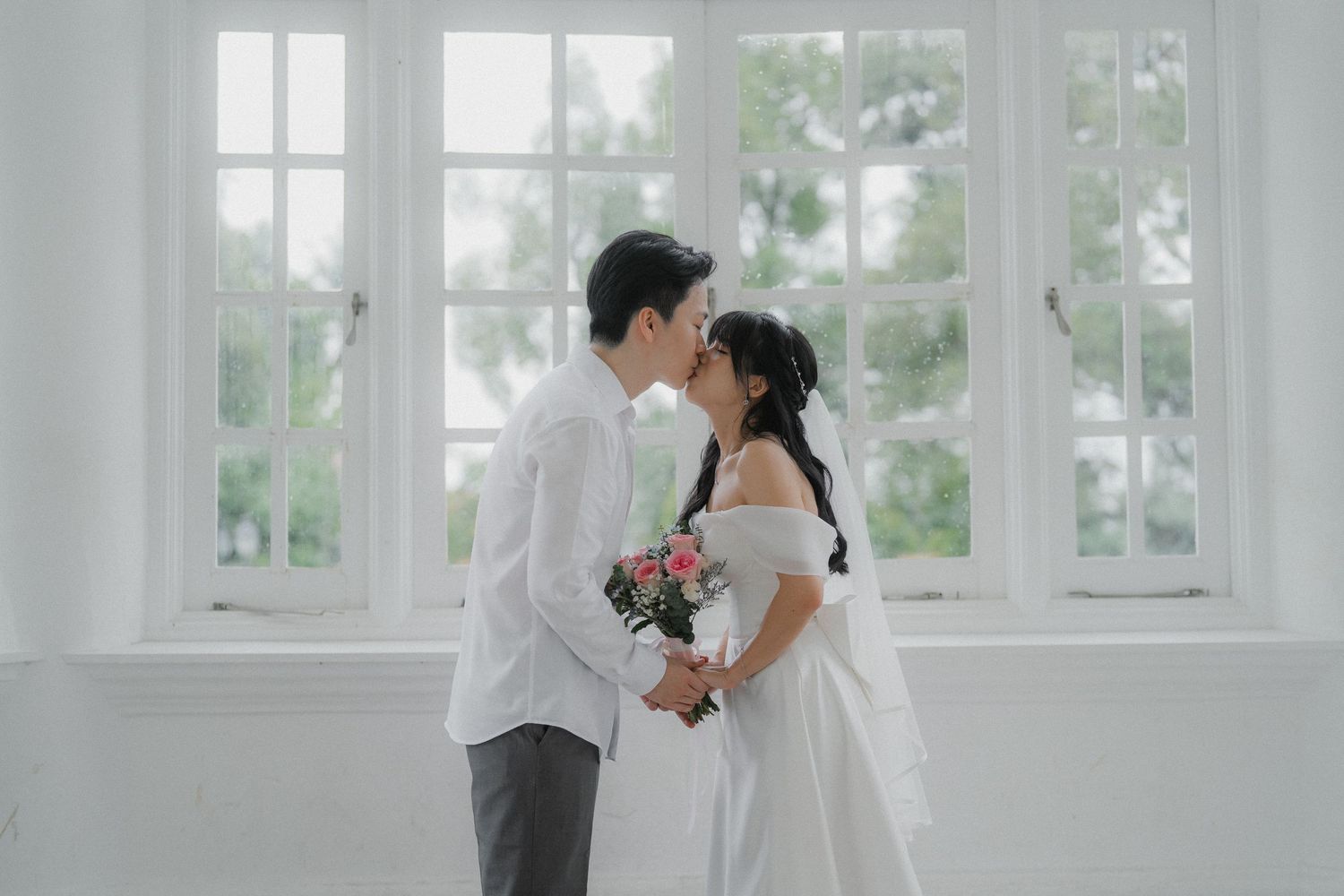 A bright white interior room with large windows and elegant architectural details creates a romantic wedding venue setting.
