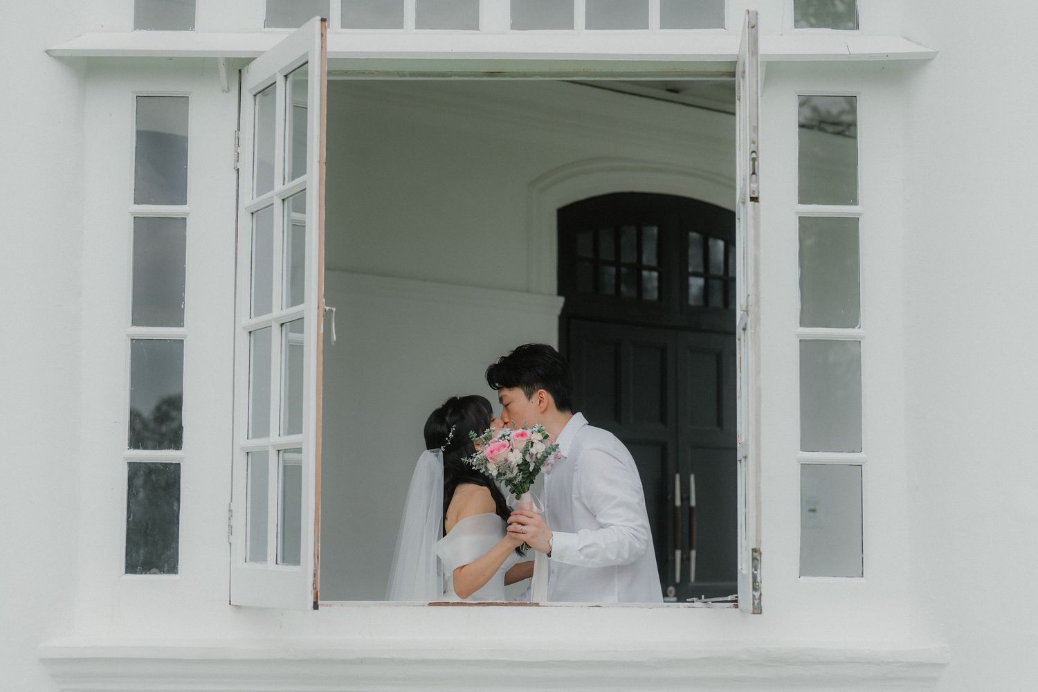 Romantic moment captured through white framed window during wedding photoshoot.
