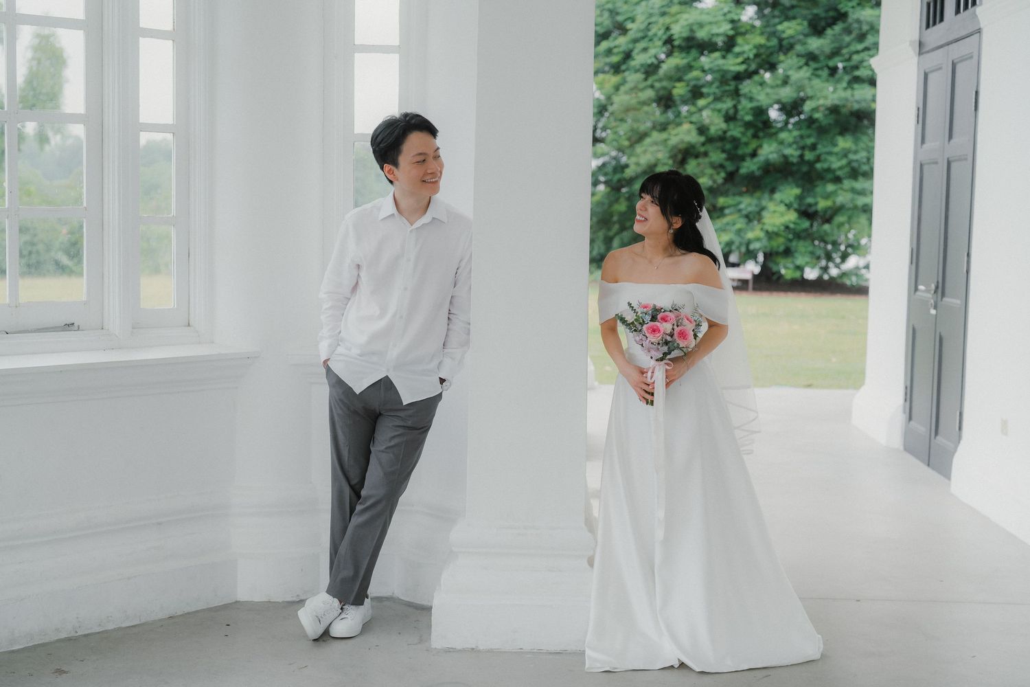 A dreamy wedding photo showing a couple in an elegant white interior with large windows.