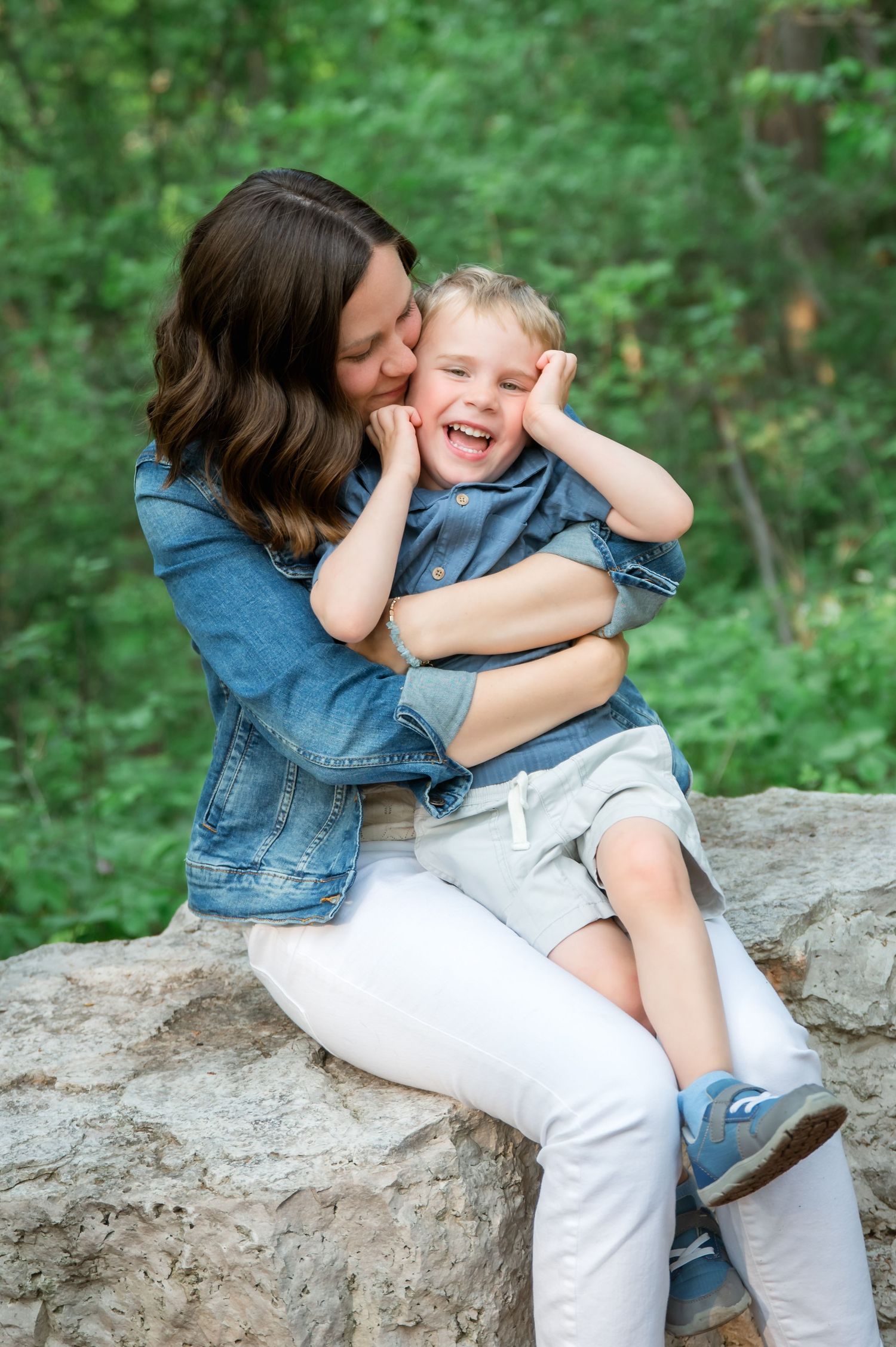 Baby in denim overalls and brown shoes stands on a winding dirt path in a lush green forest setting.