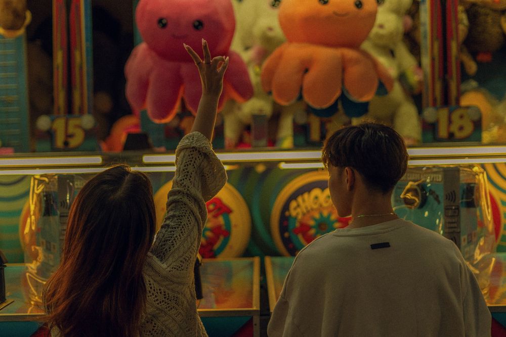 m/f couple playing a game at the fair - f is doing a peace sign high up in the air - octopus prizes in back.