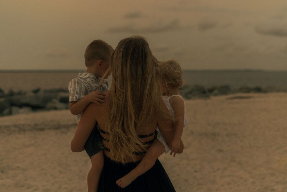 f holding her two young kids - all facing away from the camera - beach.