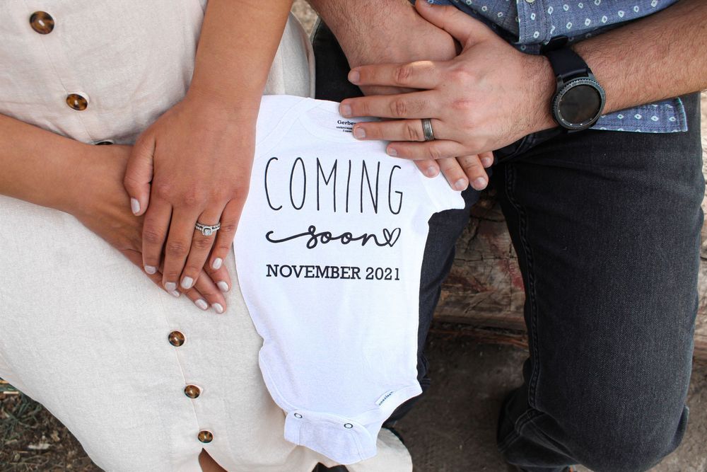 Close-up of baby onesie and sonogram held between couple during in-home pregnancy announcement session