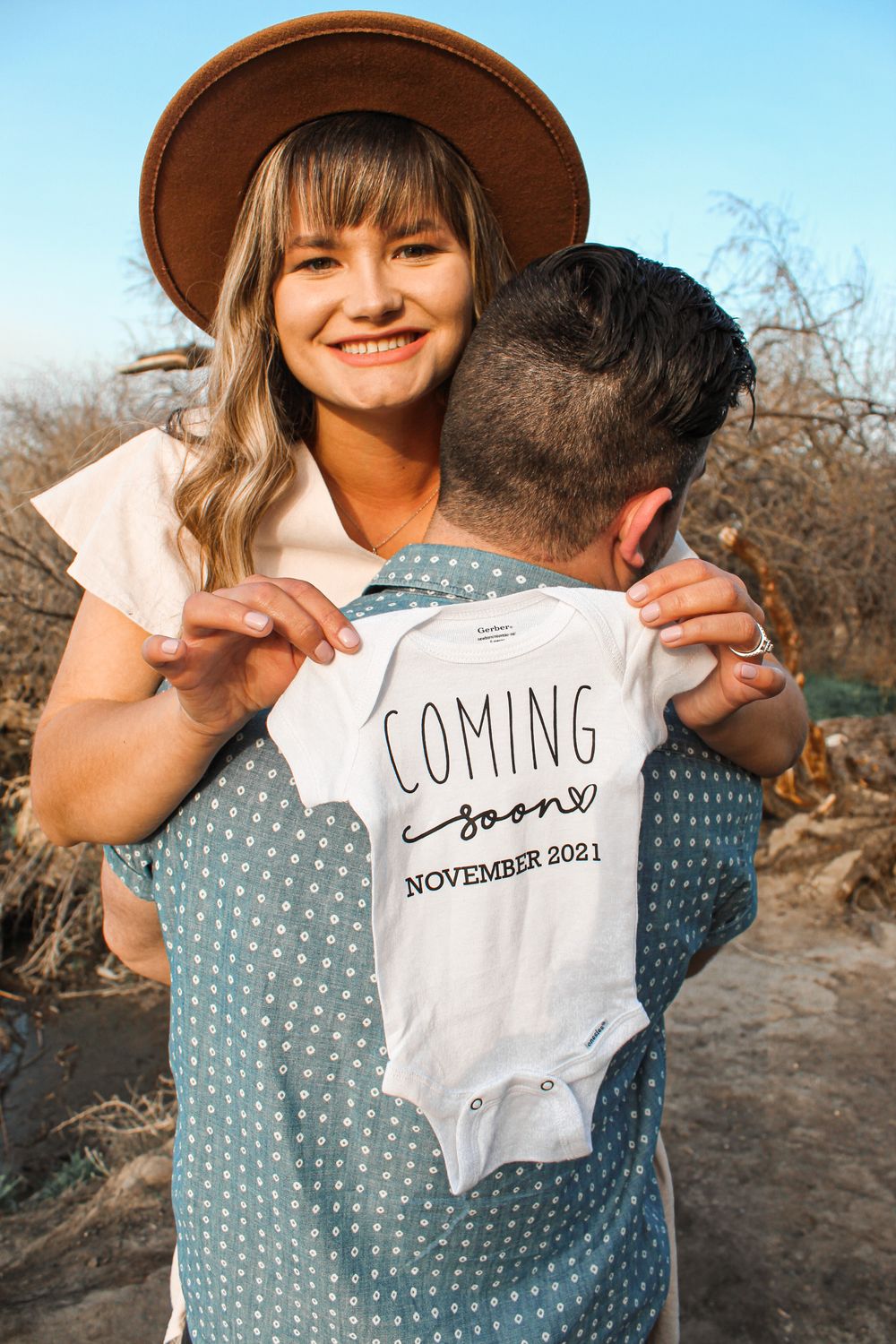 Couple smiling and holding sign that says “Coming Soon” during pregnancy announcement session in Tri-Cities WA