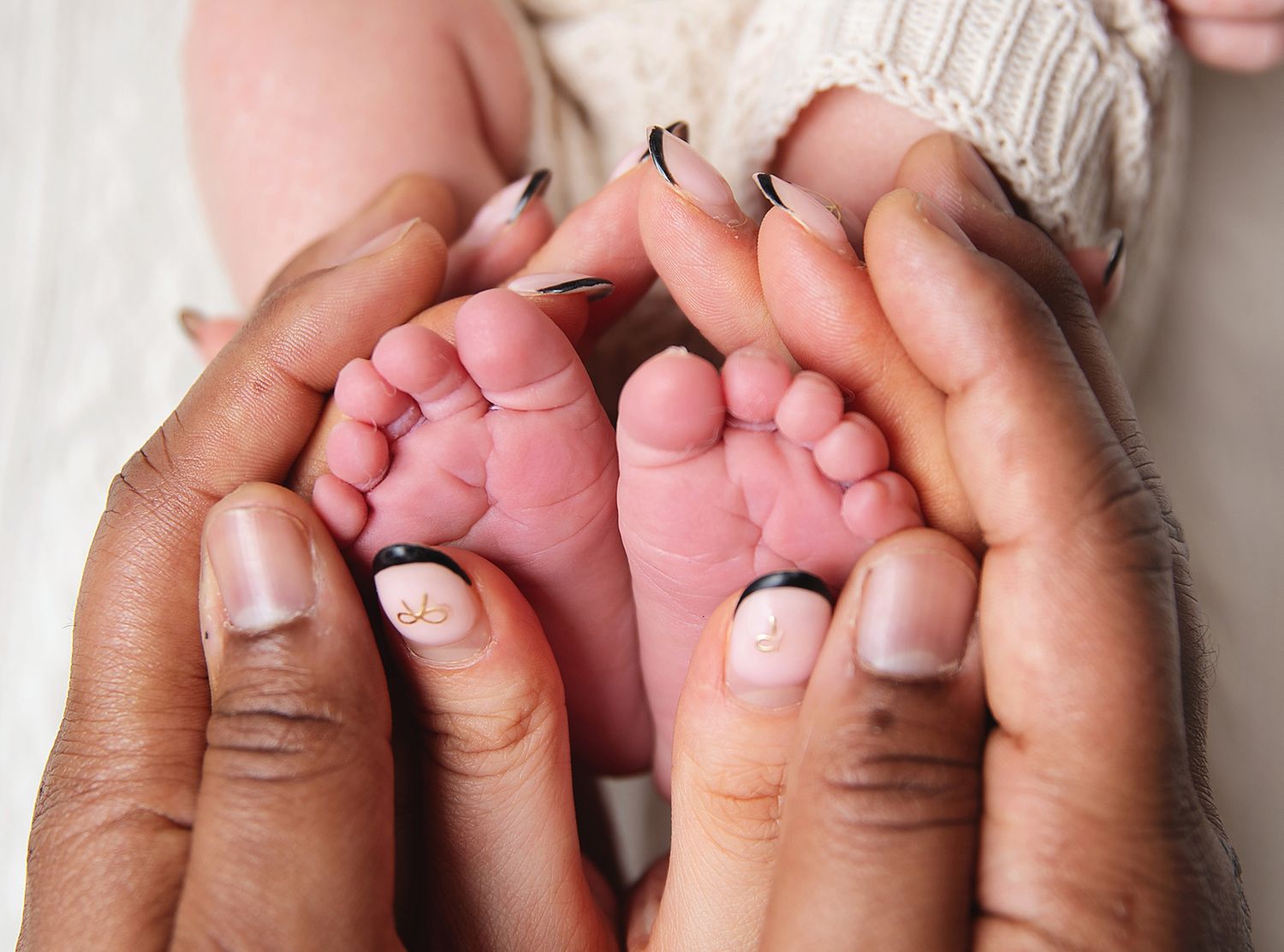 Adult hands gently holding tiny pink baby feet against a white knit fabric background.