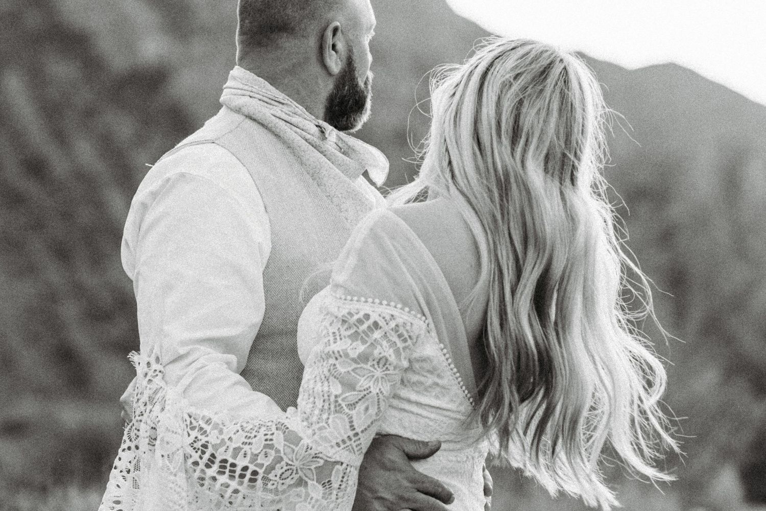 A romantic black and white wedding photo series showing a couple embracing in a meadow with mountains behind them.