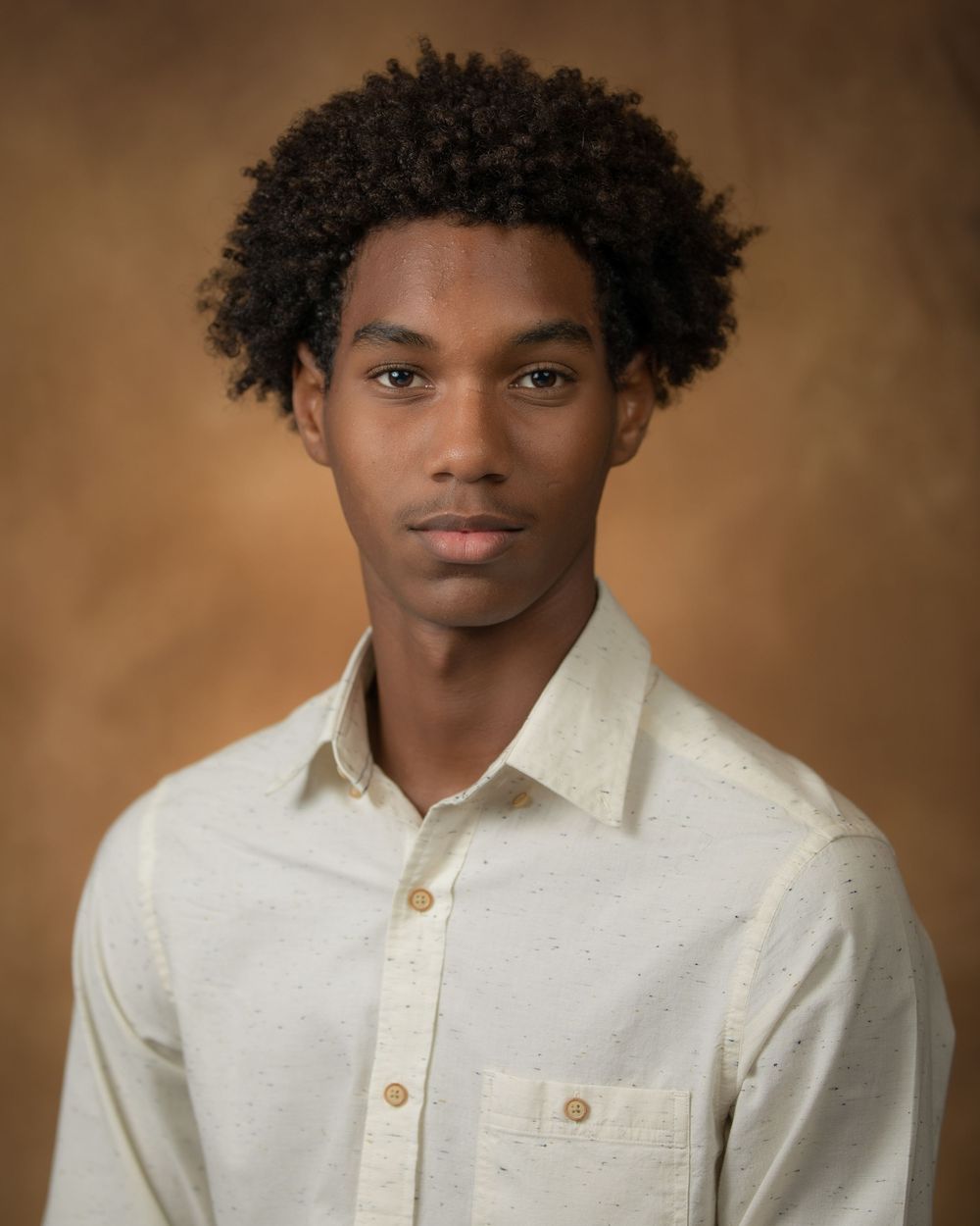 Professional headshot of person in white button-down shirt against brown backdrop.