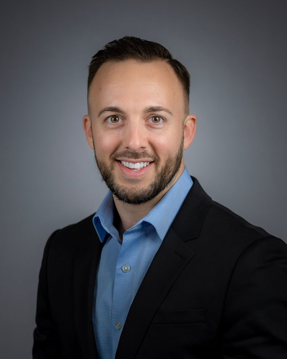 Professional headshots showing different poses with a dark background and blue shirt under black blazer.