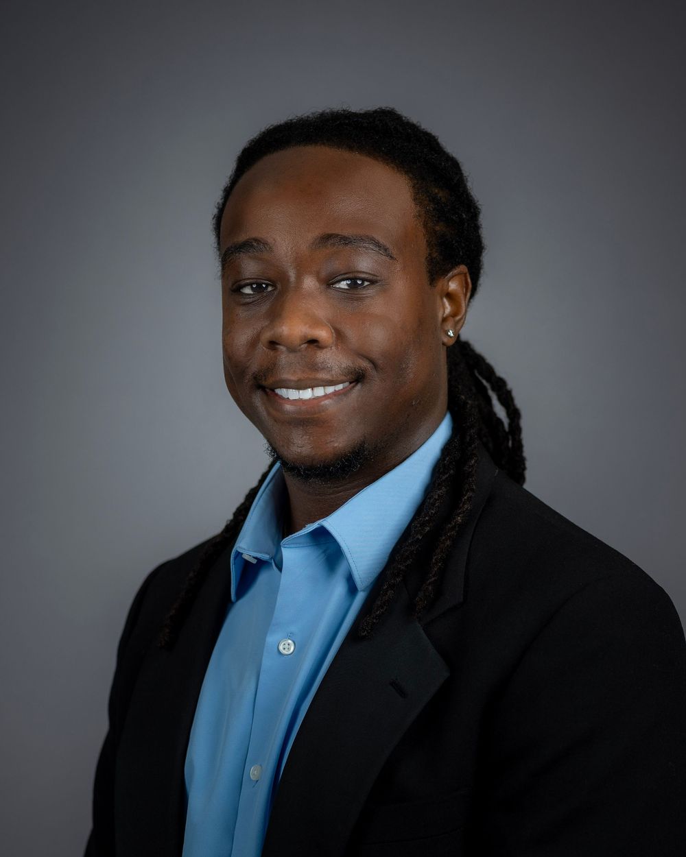 Professional portrait of person with dreadlocks wearing blue shirt and black blazer.