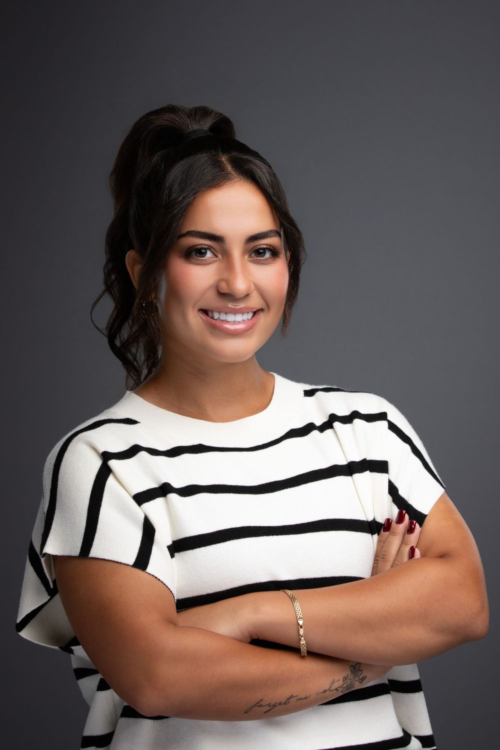 Professional woman in striped top smiling with arms crossed against gray background.