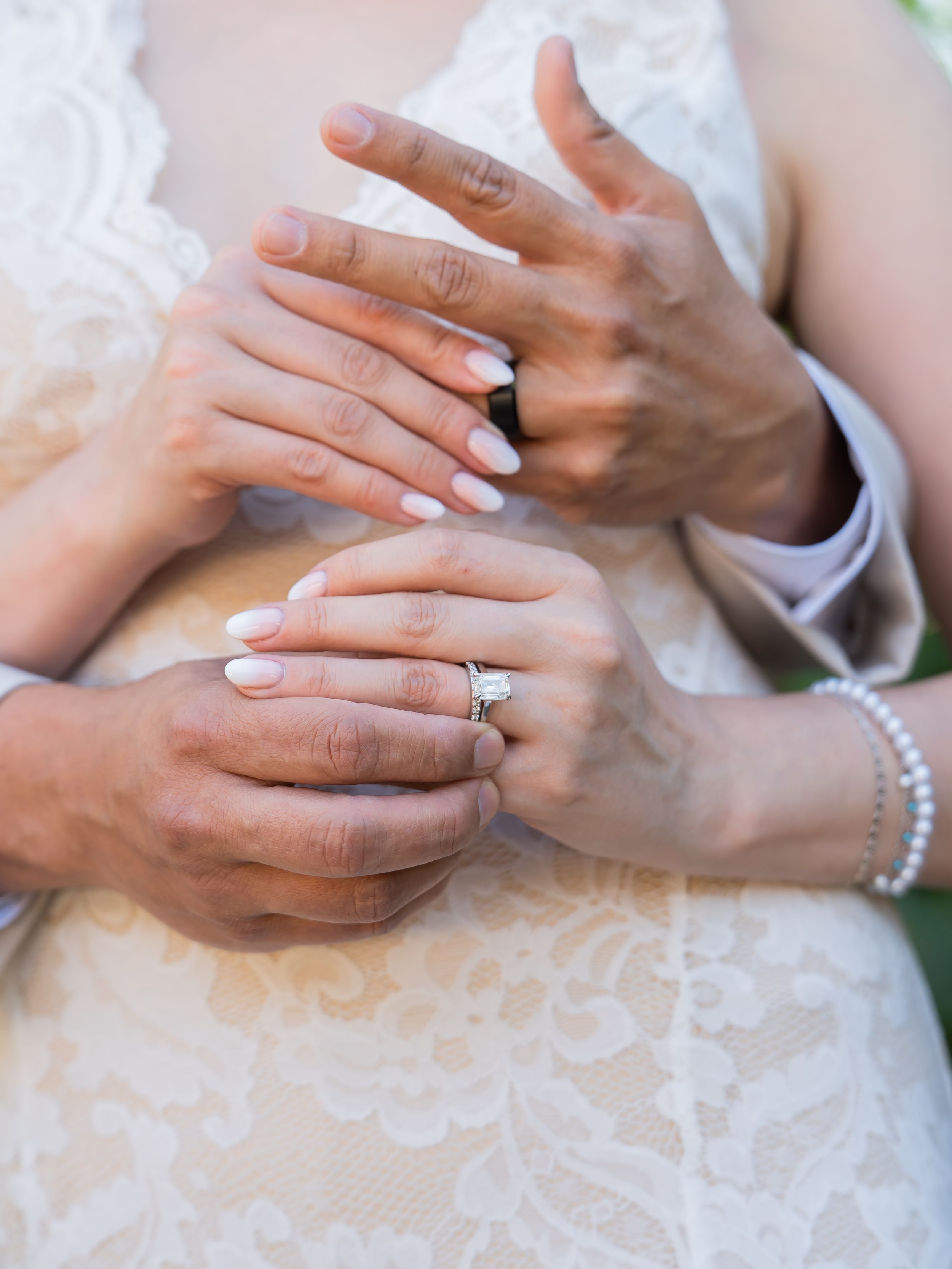 Hands with wedding rings and pearl bracelet join together showing delicate romance on a white lace background.