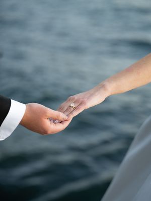 Two hands gently touching with a sparkling engagement ring against a blurred water background.