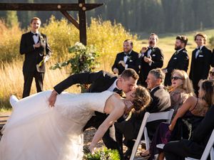 A wedding ceremony at sunset with a dramatic dip kiss between newlyweds while guests and wedding party look on.