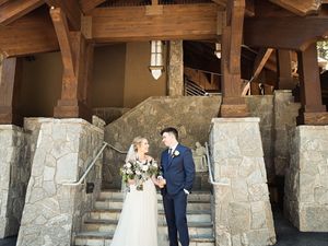 A bride and groom stand together at rustic stone and wooden beam entrance to a mountain lodge.