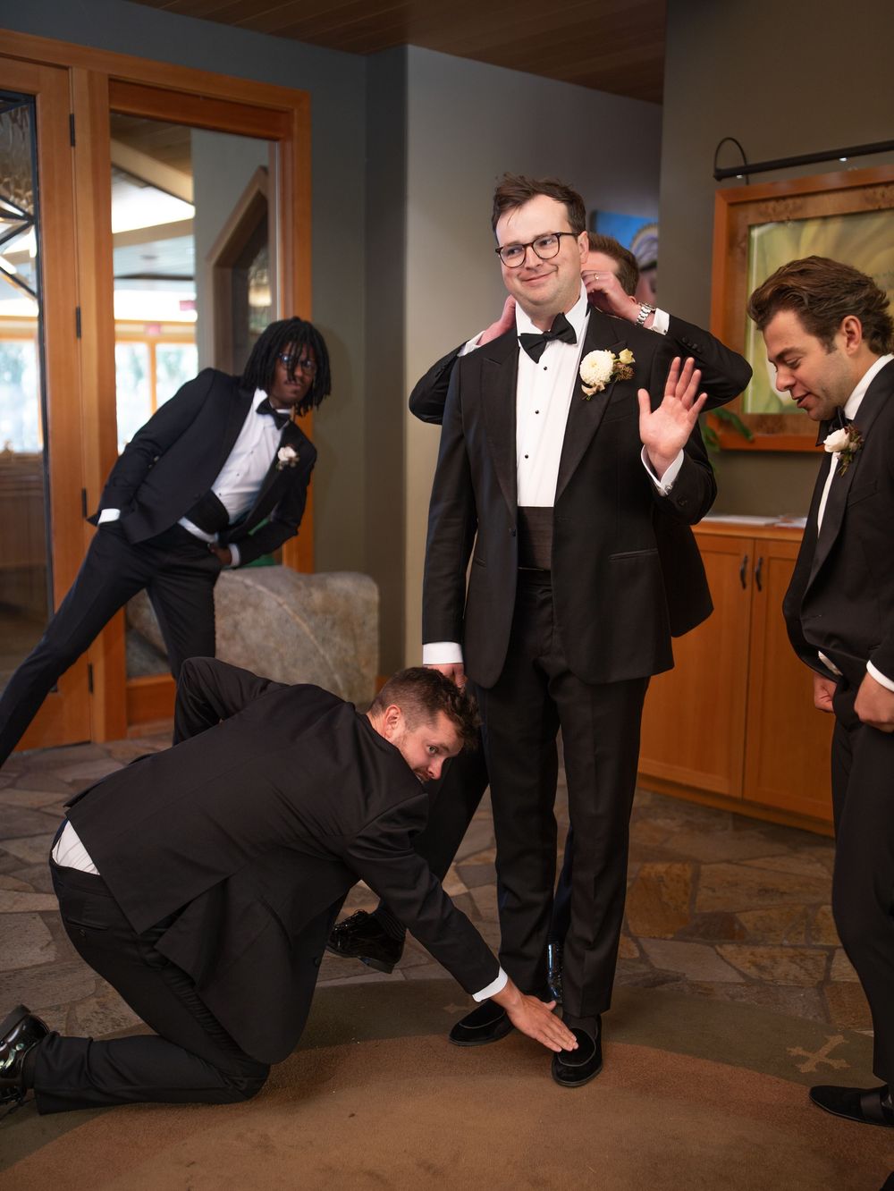 A sequence of photos shows groomsmen in black suits playfully pretending to fall down in a domino effect at a wedding.
