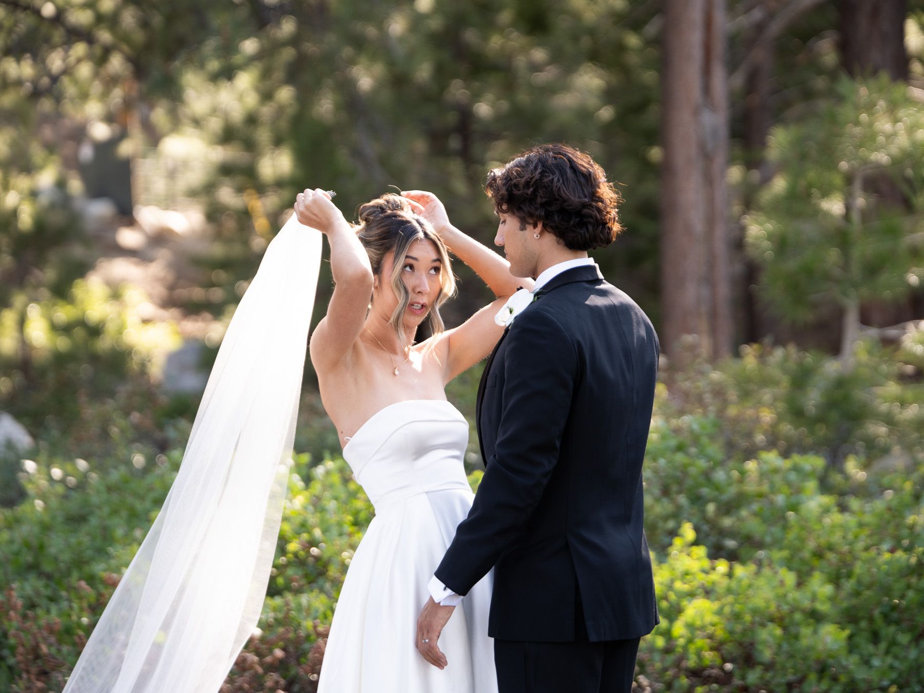 A wedding couple shares a tender moment while dancing in a scenic outdoor garden setting with sunlight filtering through trees.