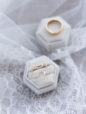 Wedding rings displayed in white hexagonal ring boxes on delicate lace fabric.