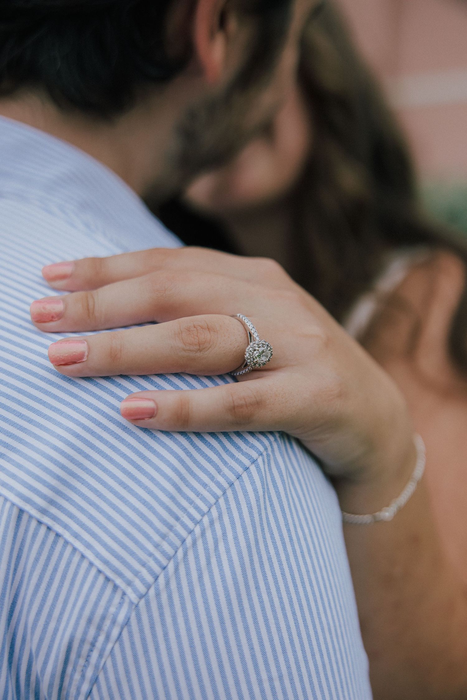 Hand with elegant vintage-style engagement ring rests on blue and white striped fabric in a romantic engagement photo.
